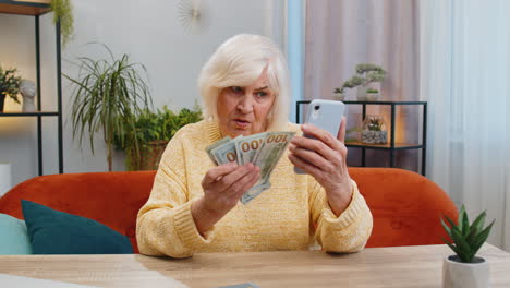 Smiling-happy-senior-grandmother-woman-counting-money-cash-use-smartphone-income-saves-lottery-win