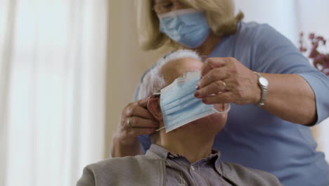 front view of mature wife putting on medical mask on husband