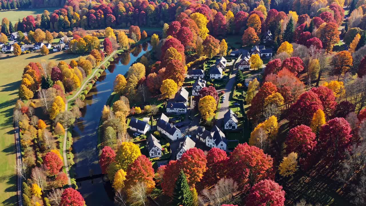 Aerial video showcasing vibrant autumn foliage surrounding a quaint village by a river