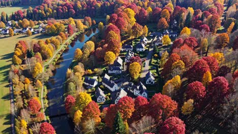Aerial video showcasing vibrant autumn foliage surrounding a quaint village by a river