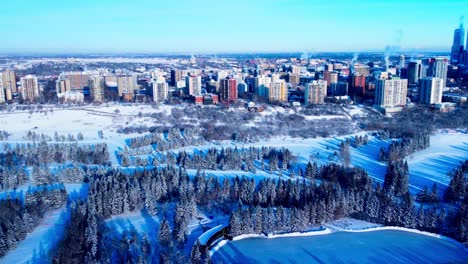 aerial edmonton downtown west revealing the city downtown high rises in the background and in the foreground the river park snow covered pine trees public outdoor skating rink cross country skiing