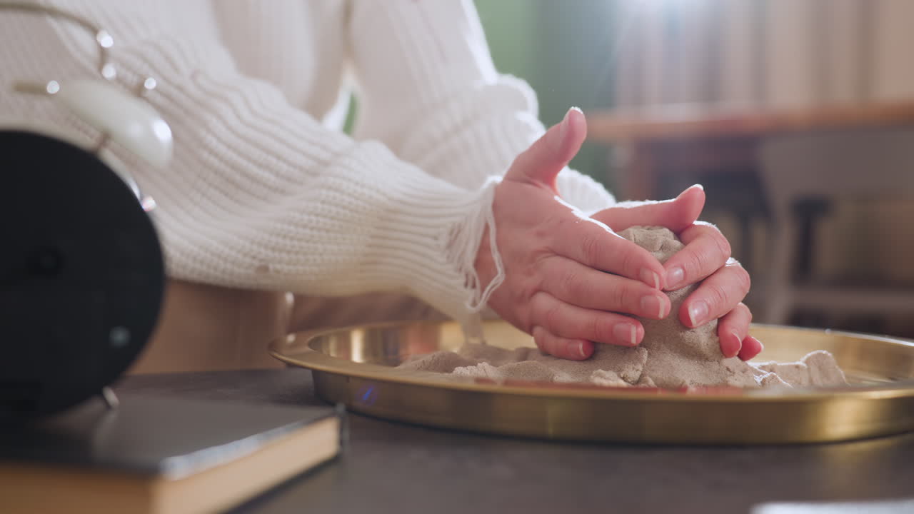Hand view of individual carefully molding soft material into octopus shape on golden tray during mindfulness therapy session, capturing tactile engagement and peaceful atmosphere in indoor setting