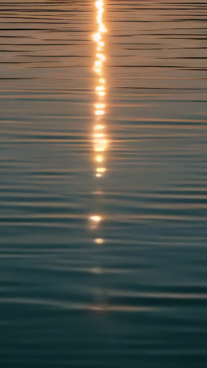 Vertical video: Pulsing vertical light column breaking into sparks as ripple bands cross calm lake
