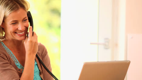jonge vrouw met laptop die aan het praten is en aan het lachen is op de telefoon