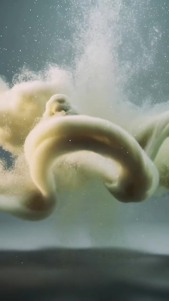 Vertical video: Releasing pale plume, spherical droplet descending in clear tank, forming tendrils