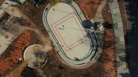 Aerial-top-down-rising-over-people-skating-in-rink-in-autumnal-publick-park-in-Los-Dominicos,-Santiago,-Chile