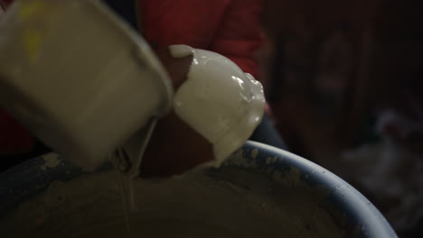 unrecognized woman pouring paint on product in workshop. artist painting pot