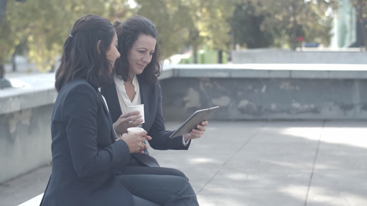 colegas mujeres sentadas al aire libre, bebiendo café y hablando