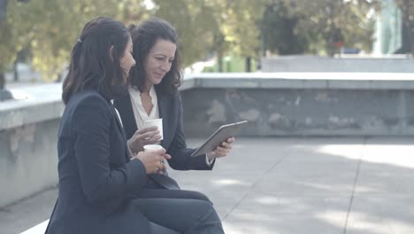 female colleagues sitting outdoors, drinking coffee and talking