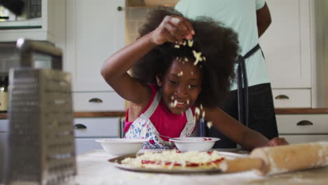 african american daughter making pizza in kitchen her father cooking in background