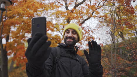 varón de raza mixta con barba en una llamada de video telefónica al aire libre durante la temporada de otoño con paisaje forestal en el fondo