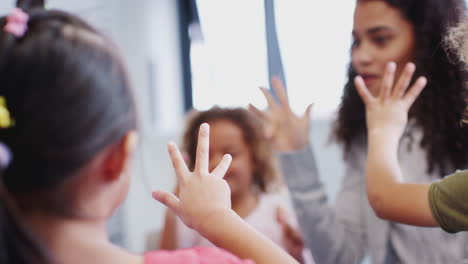 Primer-Plano-De-Niños-De-Escuela-Infantil-Y-Maestros-Contando-Con-Las-Manos-Levantadas-En-Clase,-Enfoque-Selectivo