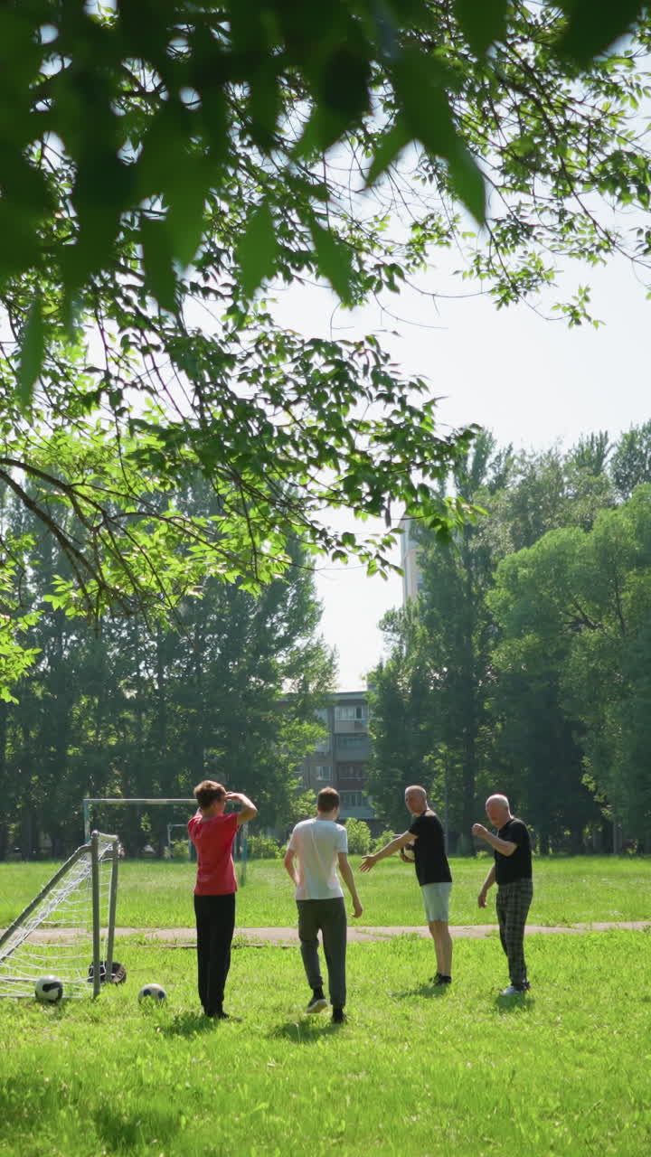 두 명의 노인이 골포스트 앞에 서서, 어린 소년에게 포스트 에 자신을 배치하도록 지시하고, 그 남자는 손에 공을 들고 있습니다.