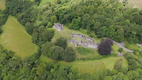 Aerial-orbital-view-of-Okehampton-Castle-surrounded-by-dense-woodland-in-Devon,-UK