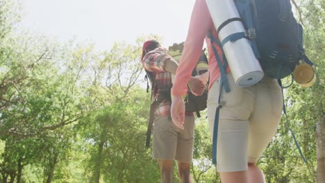 Diverse-couple-hiking-with-backpacks-and-holding-hands-in-park,-slow-motion
