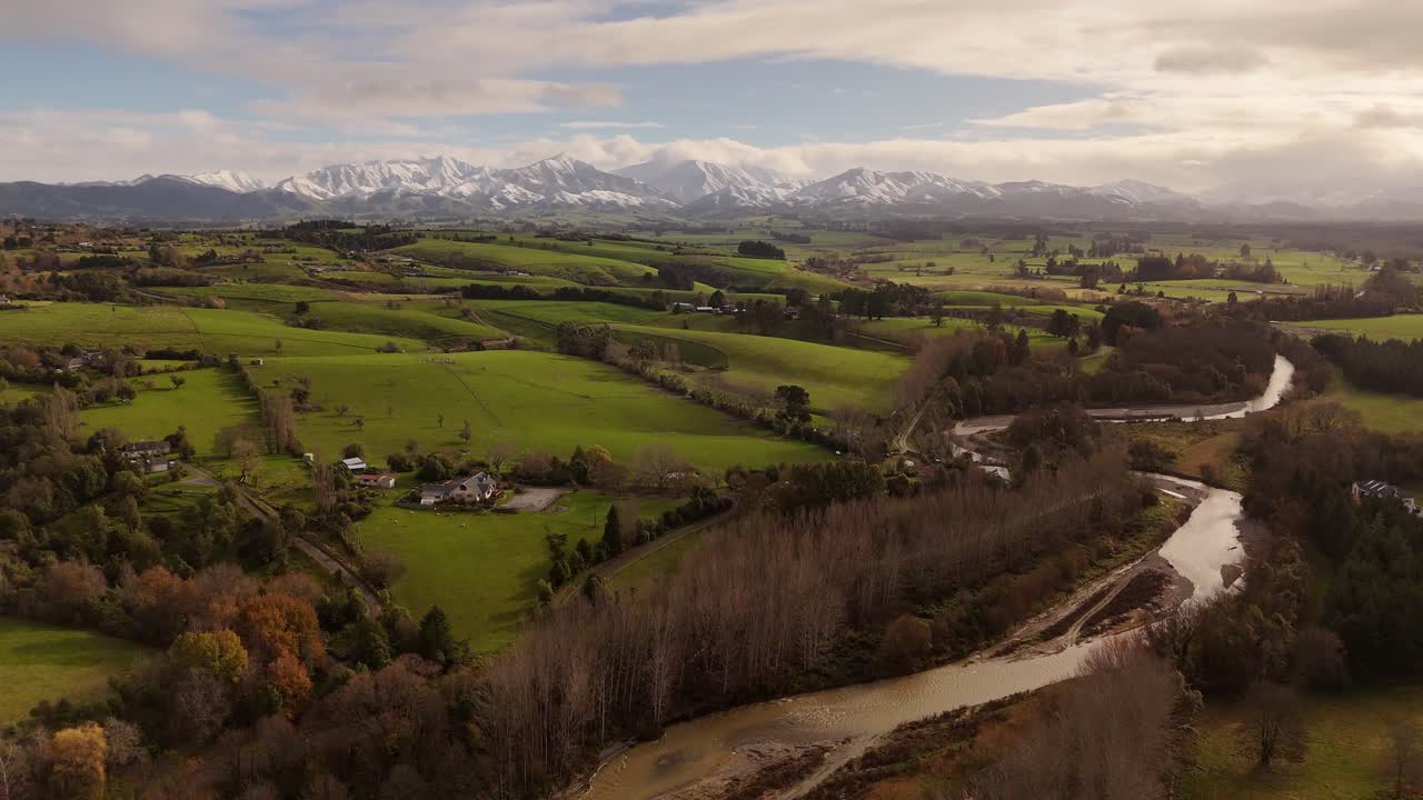 Te Moana River, lush green rolling hills and majestic snow-capped Southern Alps, Canterbury, New Zealand. Aerial backward
