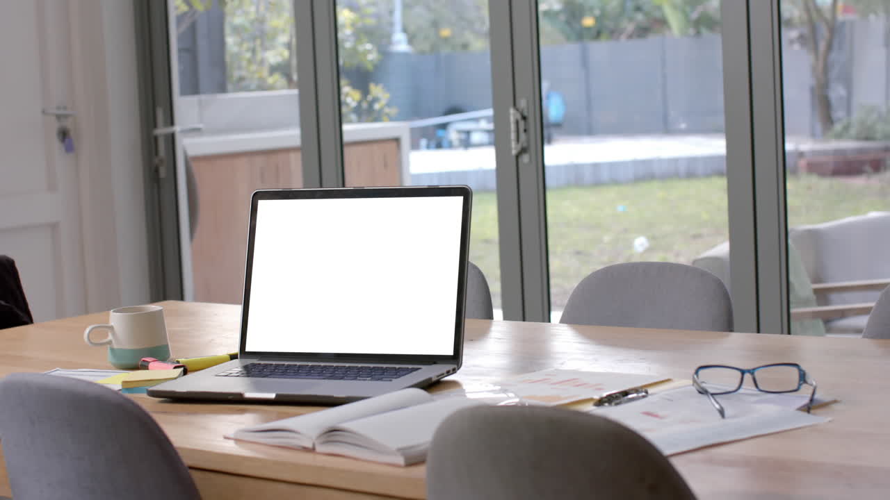 Laptop with copy space on screen, glasses and paperwork on dining table, slow motion