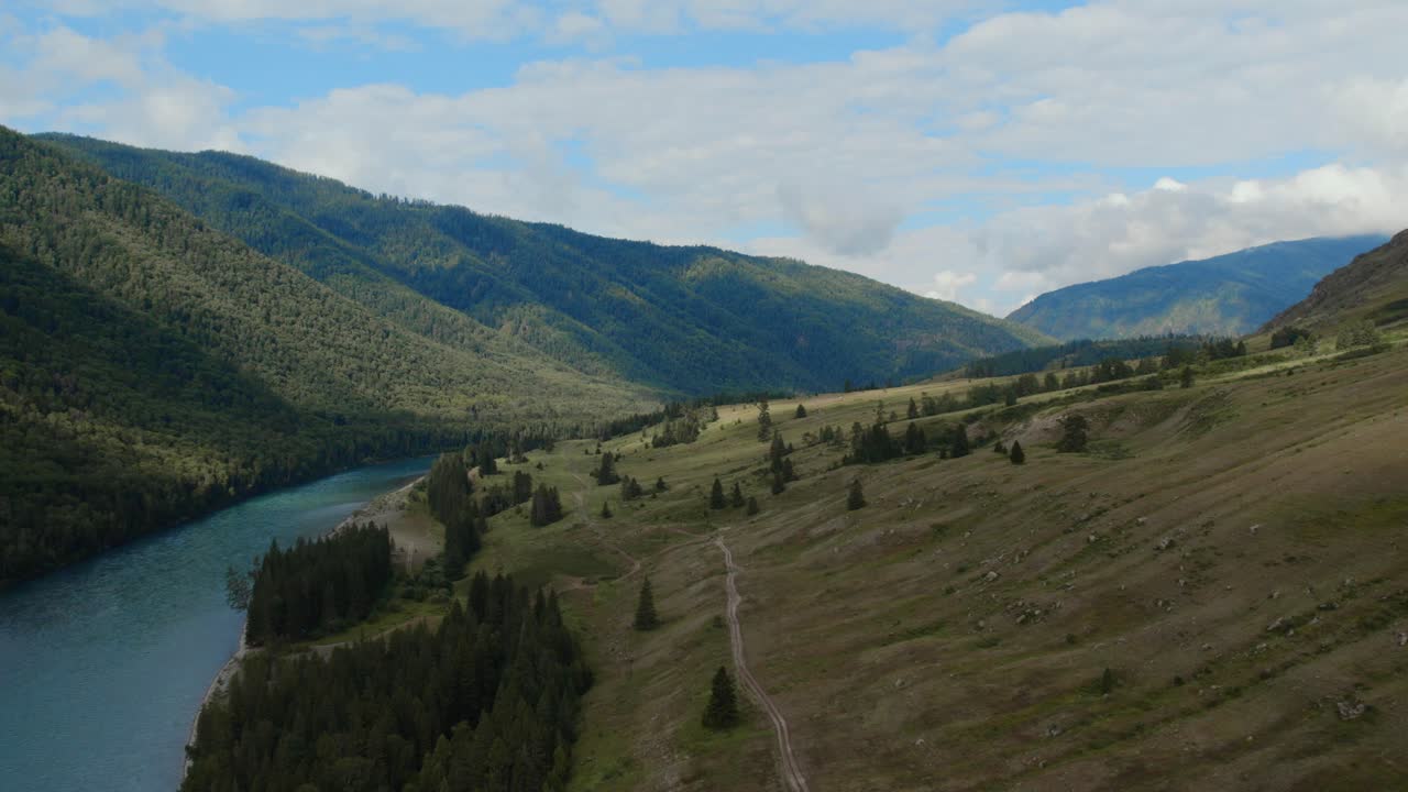 Riprese con drone della valle di Ak-Kem con un fiume turchese serpeggiante, una foresta di conifere e dolci pendii montuosi sotto un cielo blu nuvoloso nella Repubblica dell'Altai, Russia