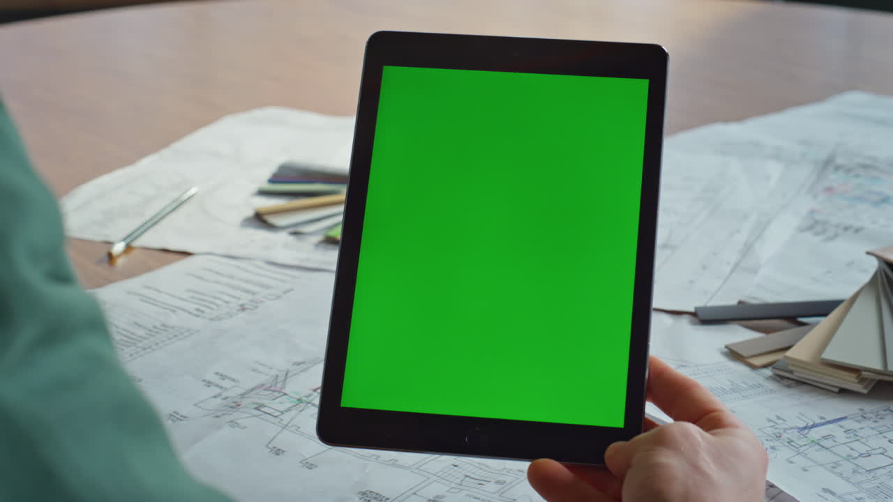 Hand holding green screen tablet watching video at corporate workplace closeup