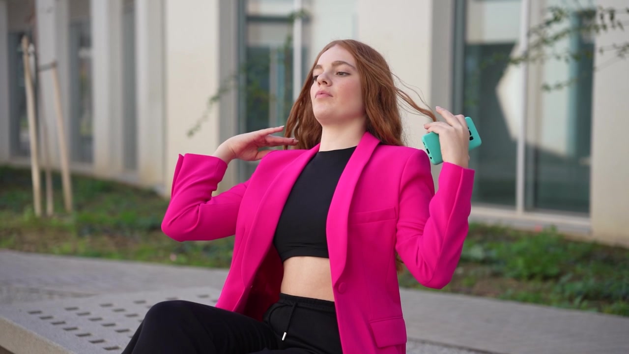En kvinde klædt i en stilfuld pink blazer betragter eftertænksomt en smart hvid taske udenfor.