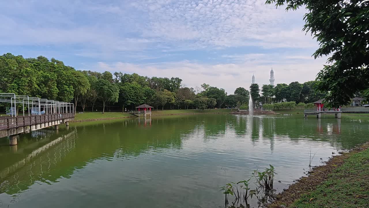 A tranquil lake in a tropical public park surrounded by lush greenery. Visitors enjoy recreation and relaxation in this serene setting.
