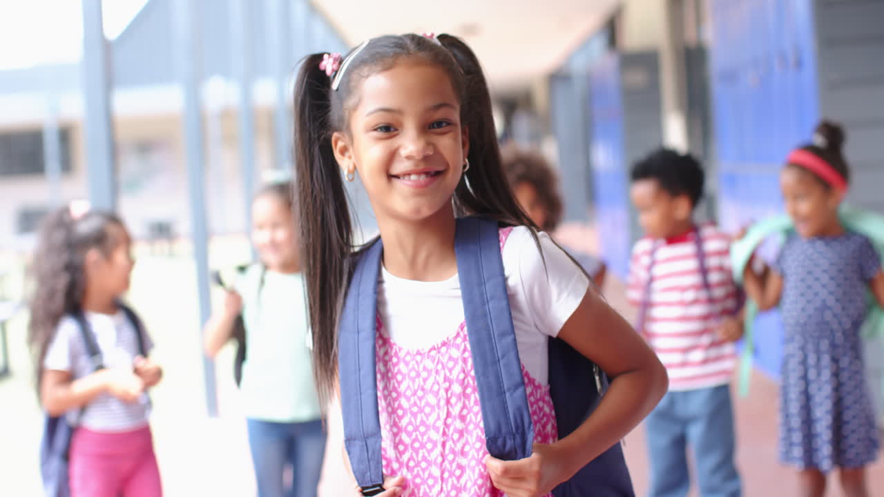 Smiling girl with backpack standing in school hallway with friends in background
