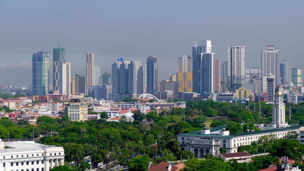 Scenic aerial pan of capital city Manila Philippines with tall high rise buildings, skyscrapers, and green parks with trees