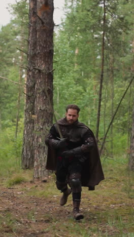 medieval warrior with cape and large sword runs to fight enemies through forest slow motion. dangerous attack of trained knight. middle age war reconstruction