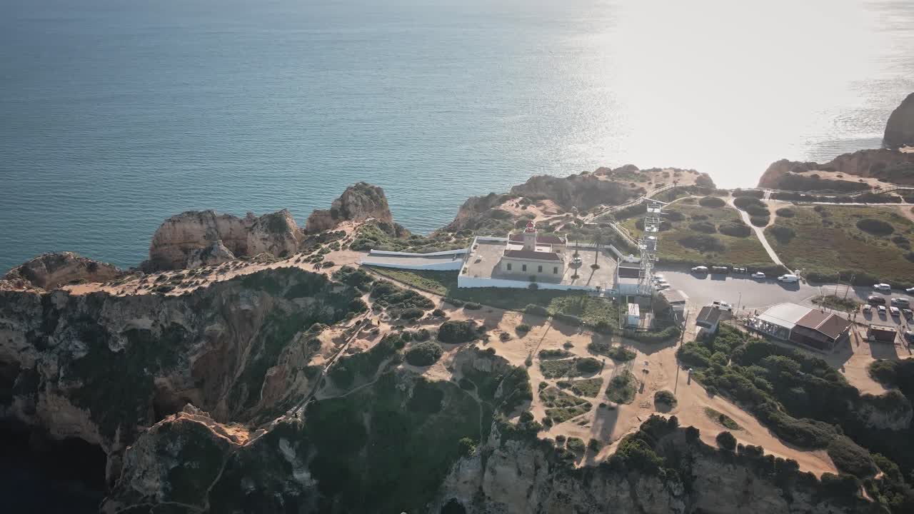 Camera spirals around Ponta da Piedade lighthouse, revealing sculpted cliffs, winding trails, and the sparkling coastline in sweeping sunlit motion