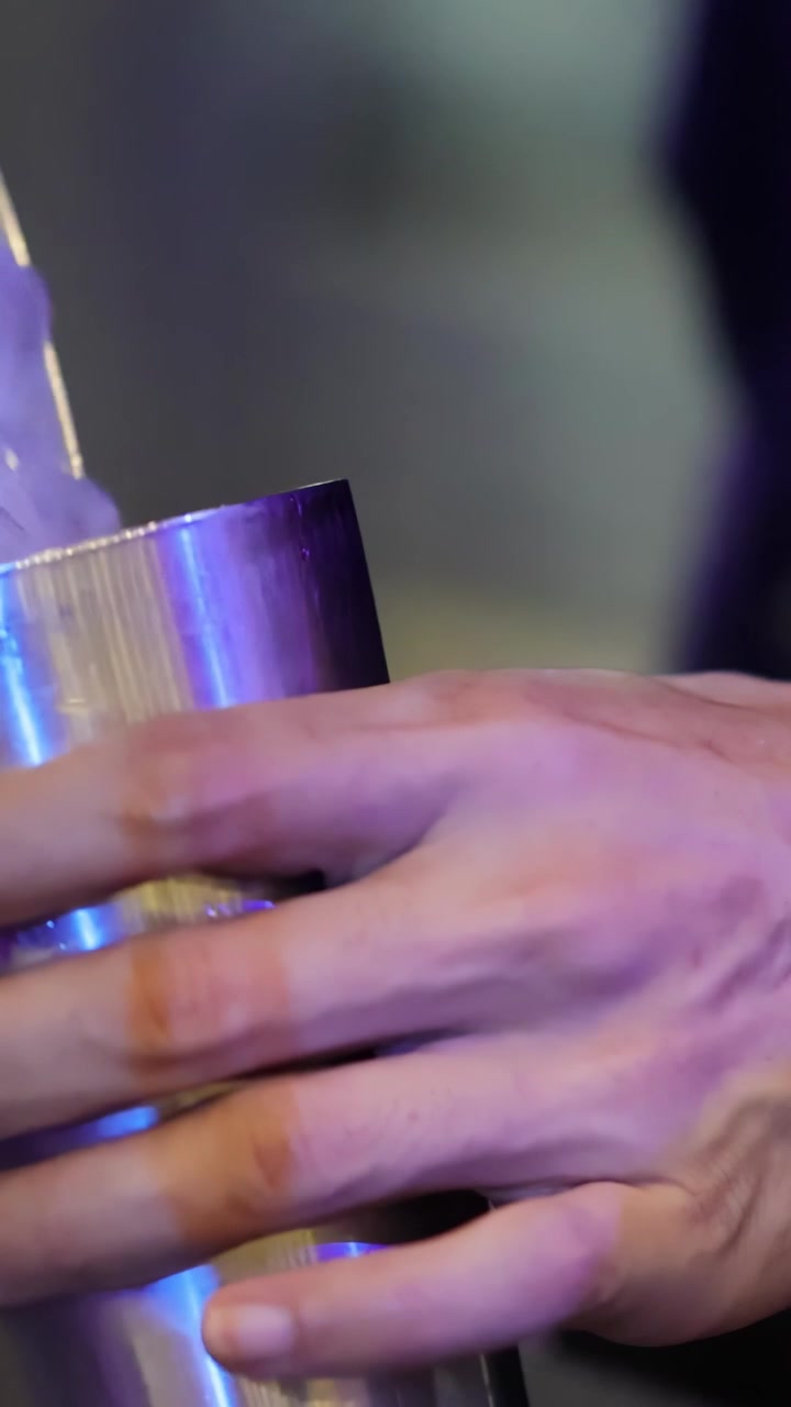 Un barista prepara un cocktail con ghiaccio nello shaker, illuminazione vivace del bar, movimento ravvicinato della telecamera a mano