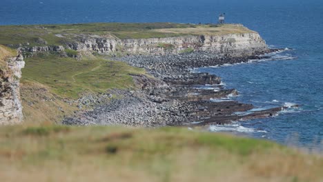 Weiches-Gras-Bedeckt-Hoch-Aufragende,-Verdorrte-Klippen-über-Der-Küste,-Während-Wellen-Auf-Den-Strand-Darunter-Rollen