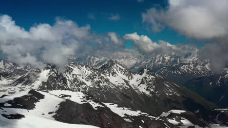 Air-flight-through-mountain-clouds-over-beautiful-snow-capped-peaks-of-mountains-and-glaciers.