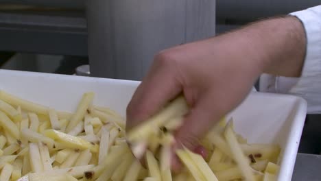 hand grabbing rejected french fries in a food factory