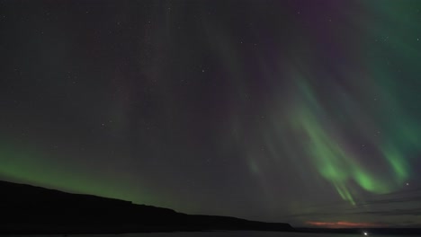 Der-Winterhimmel-Wird-Durch-Den-Wunderschönen-Tanz-Der-Aurora-Borealis-über-Dem-Dunklen,-Stillen-Wasser-Des-Fjords-Erleuchtet