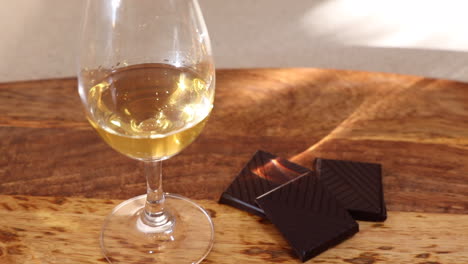 zooming out from a closeup of a glass of single malt scotch whisky, paired with squares of dark chocolate sitting on a wooden platter, with evening sunlight and shadows