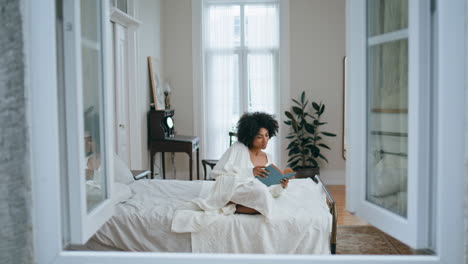 Mujer-Despreocupada-Volteando-Páginas-De-Libros-En-El-Interior.-Señora-Africana-Leyendo-Novela-Acostada-En-La-Cama.