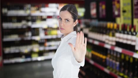 Animation-of-serious-caucasian-woman-making-stop-hand-sign,-over-alcohol-for-sale-in-shop