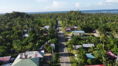Drone footage capturing a straight, peaceful road cutting through a lush tropical village on Siargao Island, Philippines. Rural charm with dense coconut palm forests and colorful tin-roof houses
