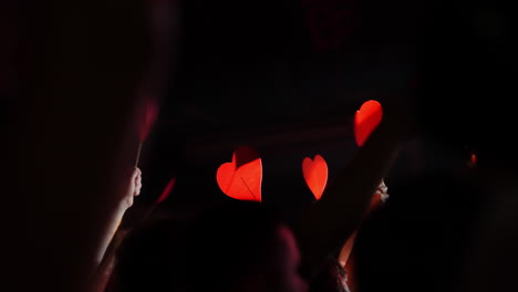 hands holding red heart-shaped signs during a lively concert with vibrant atmosphere and excitement