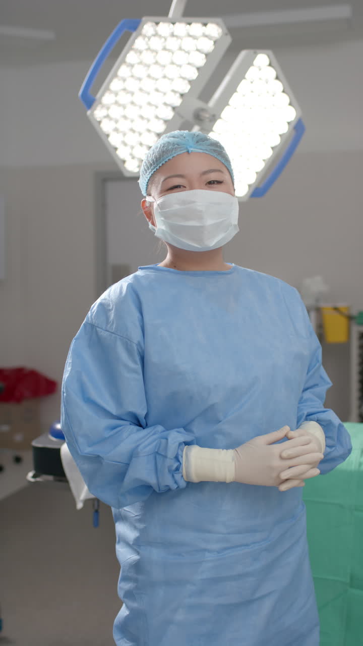 Vertical video of portrait of asian female surgeon in operating theatre, slow motion