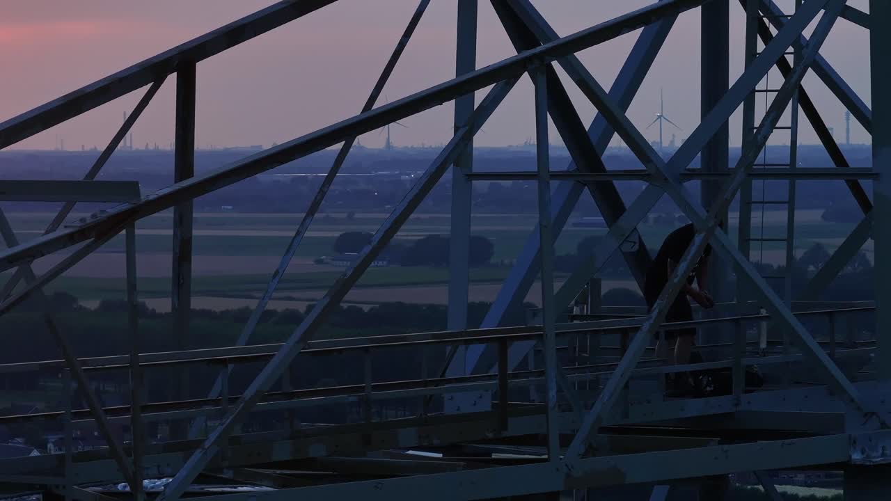 Man standing on a metal structure at sunset with a wide landscape in the background