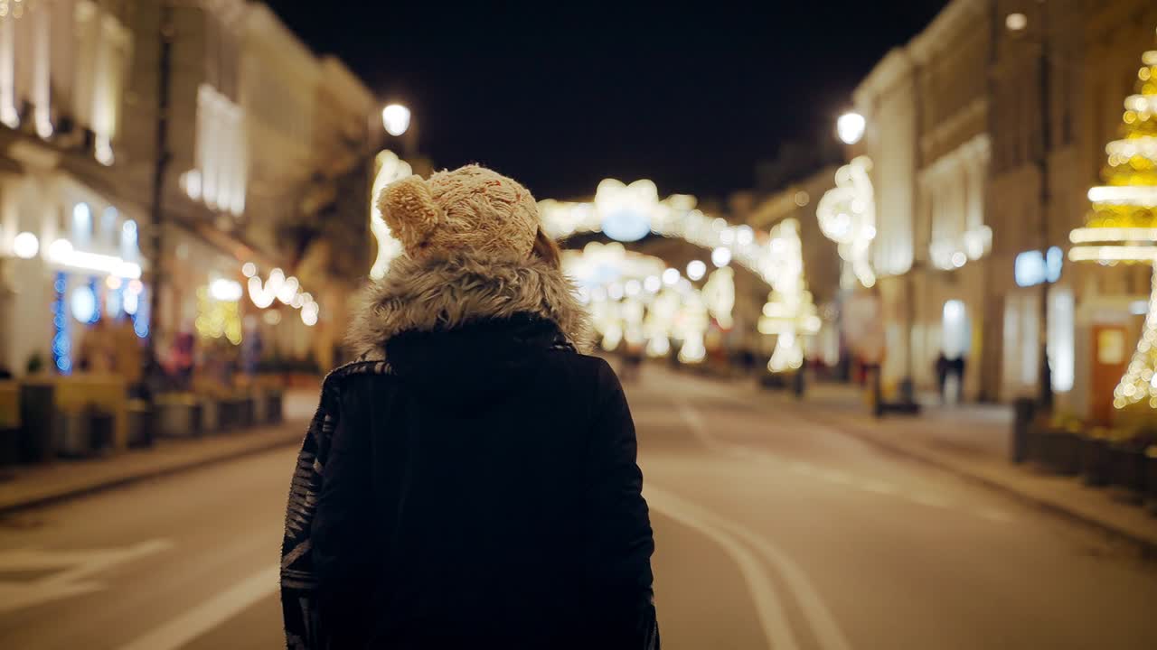크리스마스를 탐험하는 젊은 여성 관광객, 시내 광장에서 크리스마스 장식품을 향해 걸어가는 관광객, 겨울에 밤에 거리에서 행복하게 걸어가는 여성의 뒷면 영상.