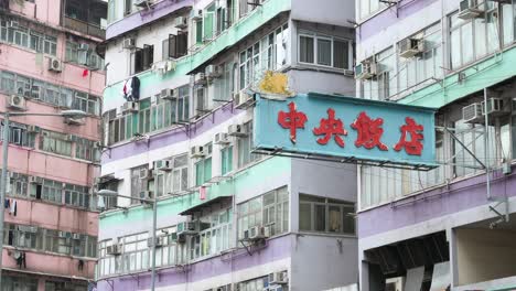 a street neon sign hangs from a facade of a colorful residential building in hong kong