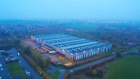 warehouse at dusk: aerial moving back up, with the lights of the nearby city and roads