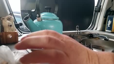 female hand igniting cooker hob under vintage steam kettle in camper van kitchen space