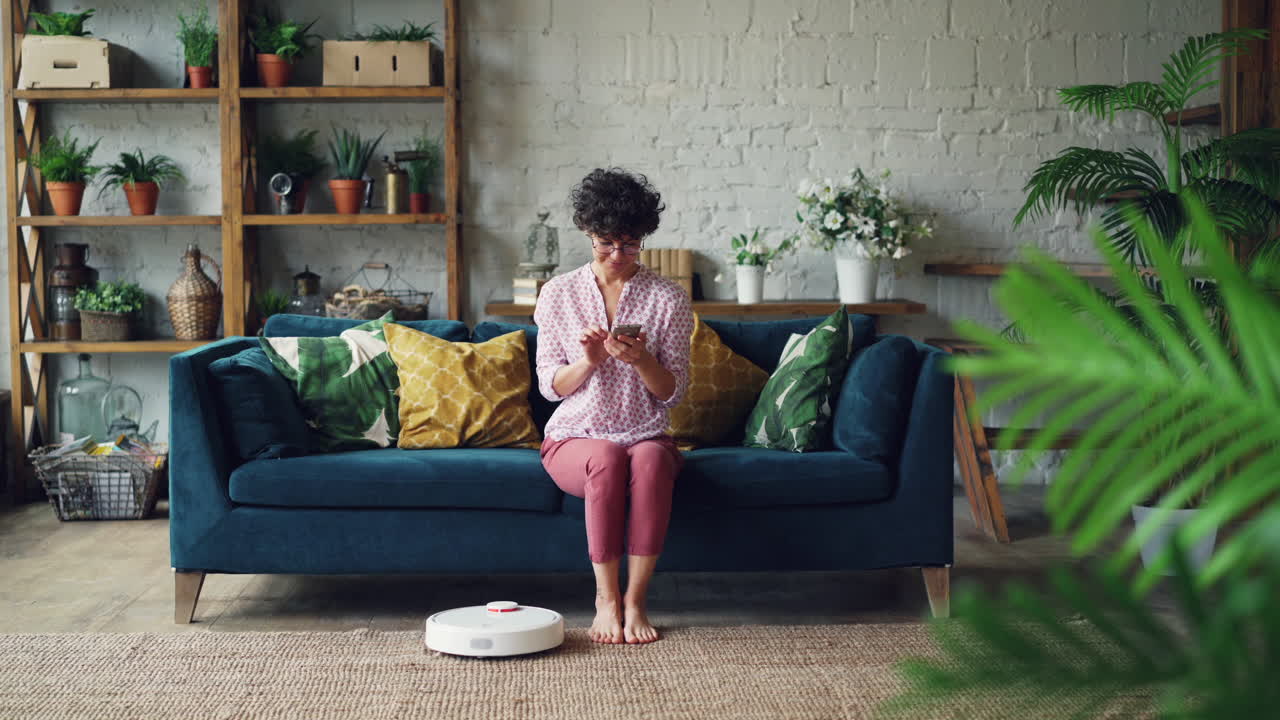 Woman using smartphone to control robot vacuum in living room