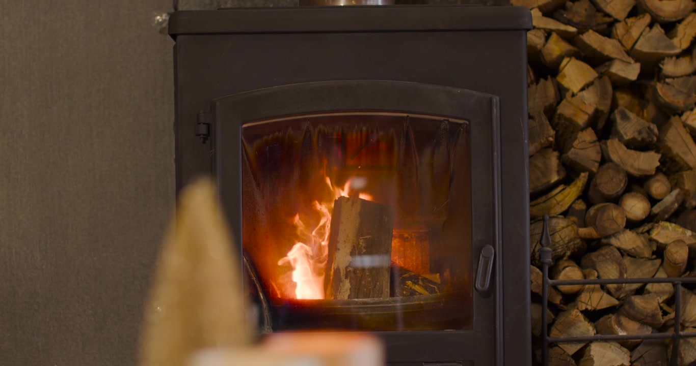 Braci ardenti accendono un tronco verticale in una stufa a legna, le fiamme salgono, carbonizzando il tronco e riscaldando la casa