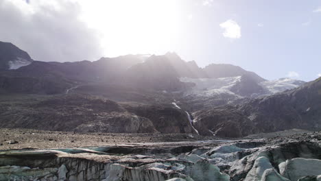 Panoramic-aerial-view-of-debris-covering-glaciers-at-the-foot-of-mountains-in-summer-daylight