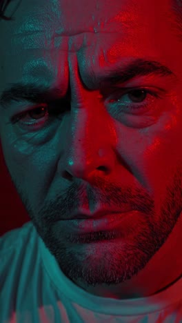 melancholy expression of a middle aged man with a beard, illuminated by intense red and blue lights, creating a dramatic and emotional atmosphere