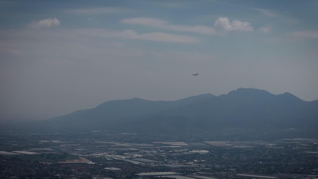 Video of an airplane in motion starting its landing at an airport in Mexico City, Mexico. Captures aviation activity, approach, and urban airport surroundings from above